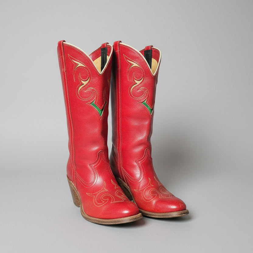 Pair of red cowboy boots with intricate designs on a decorative stand.