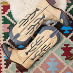 Pair of beige cowboy boots with decorative patterns on a patterned rug