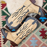 Pair of beige cowboy boots with decorative patterns on a patterned rug
