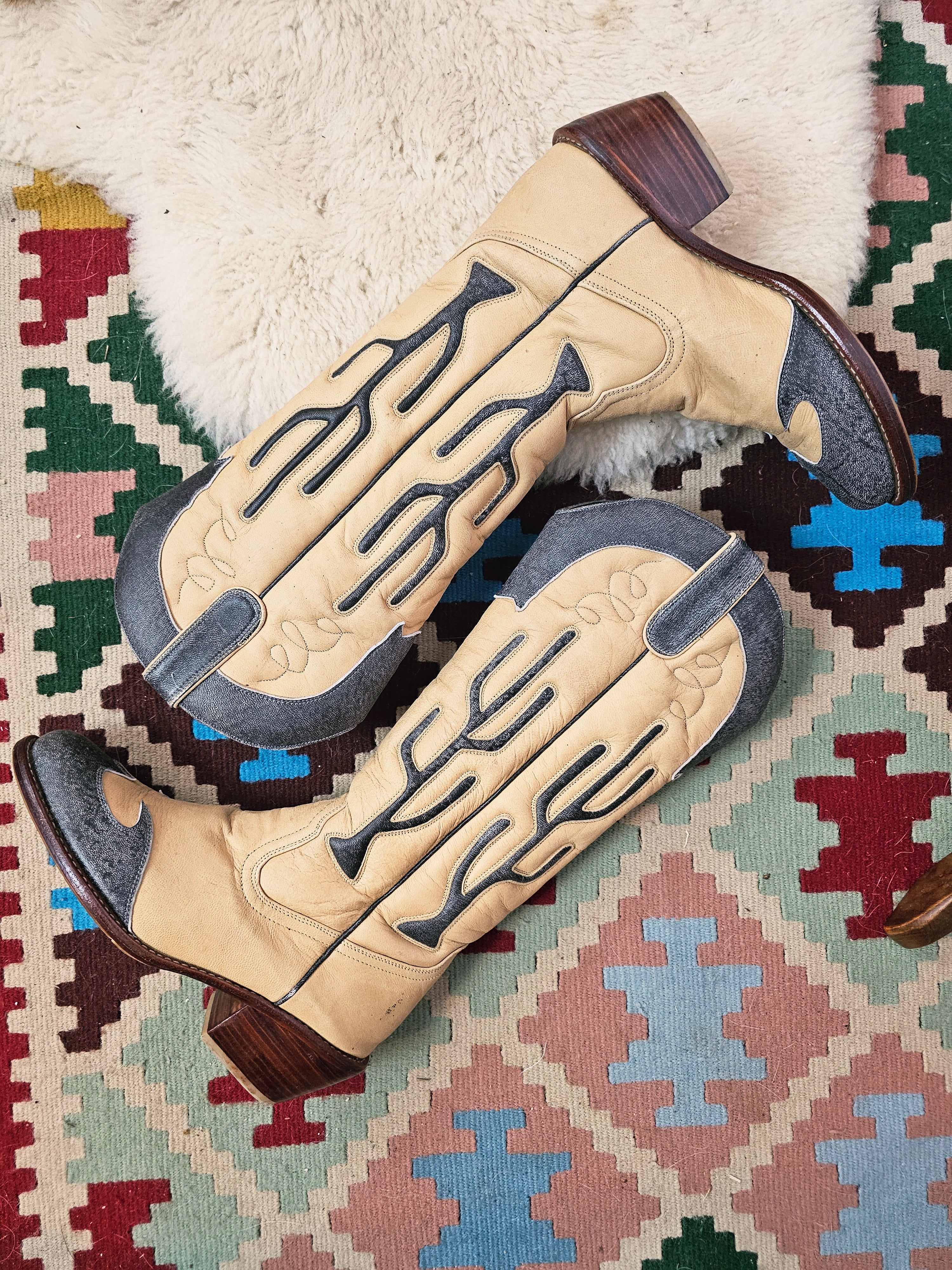 Pair of beige cowboy boots with decorative patterns on a patterned rug