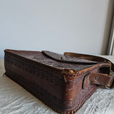 Brown leather pouch with intricate designs attached to a white surface