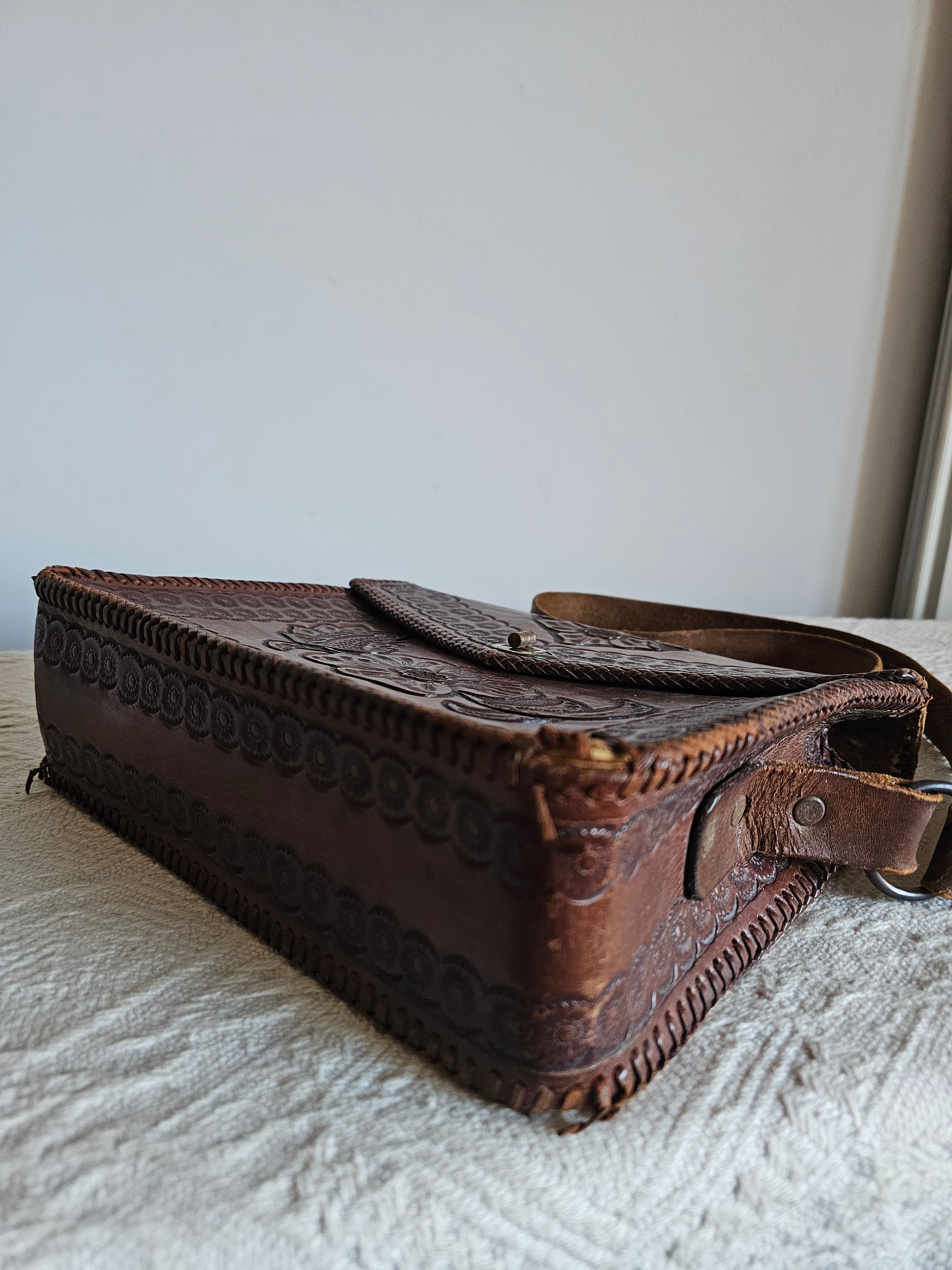 Brown leather pouch with intricate designs attached to a white surface