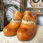 Pair of Vintage Wild Pair Tan Leather Mules – Size 37 with boho fringe and cushioned platform soles, styled on a cozy surface.