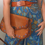 Person wearing a blue patterned outfit holding a brown leather bag.
