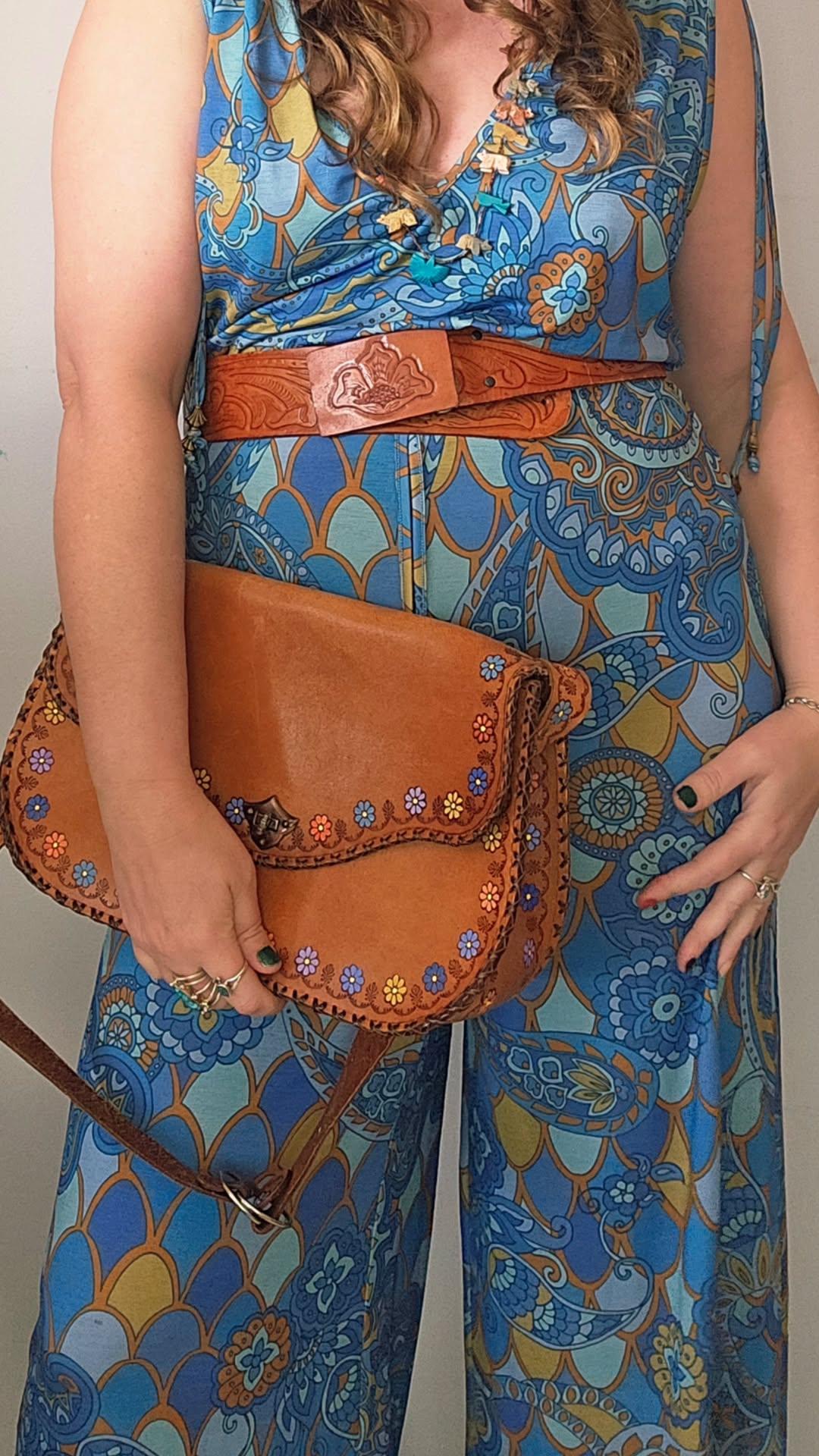 Person wearing a blue patterned outfit holding a brown leather bag.