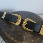 Black leather strap with gold buckles on a wooden surface