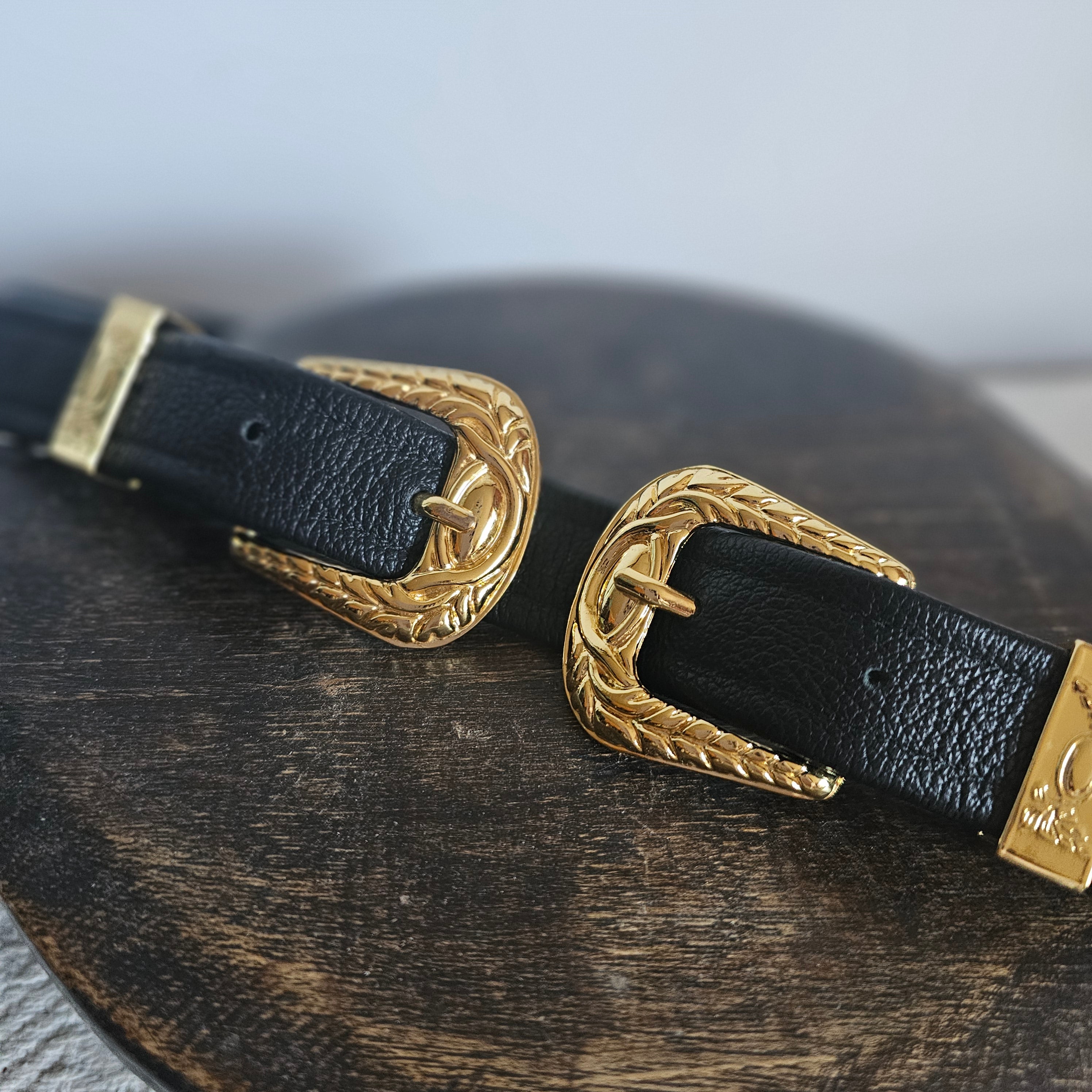 Black leather strap with gold buckles on a wooden surface