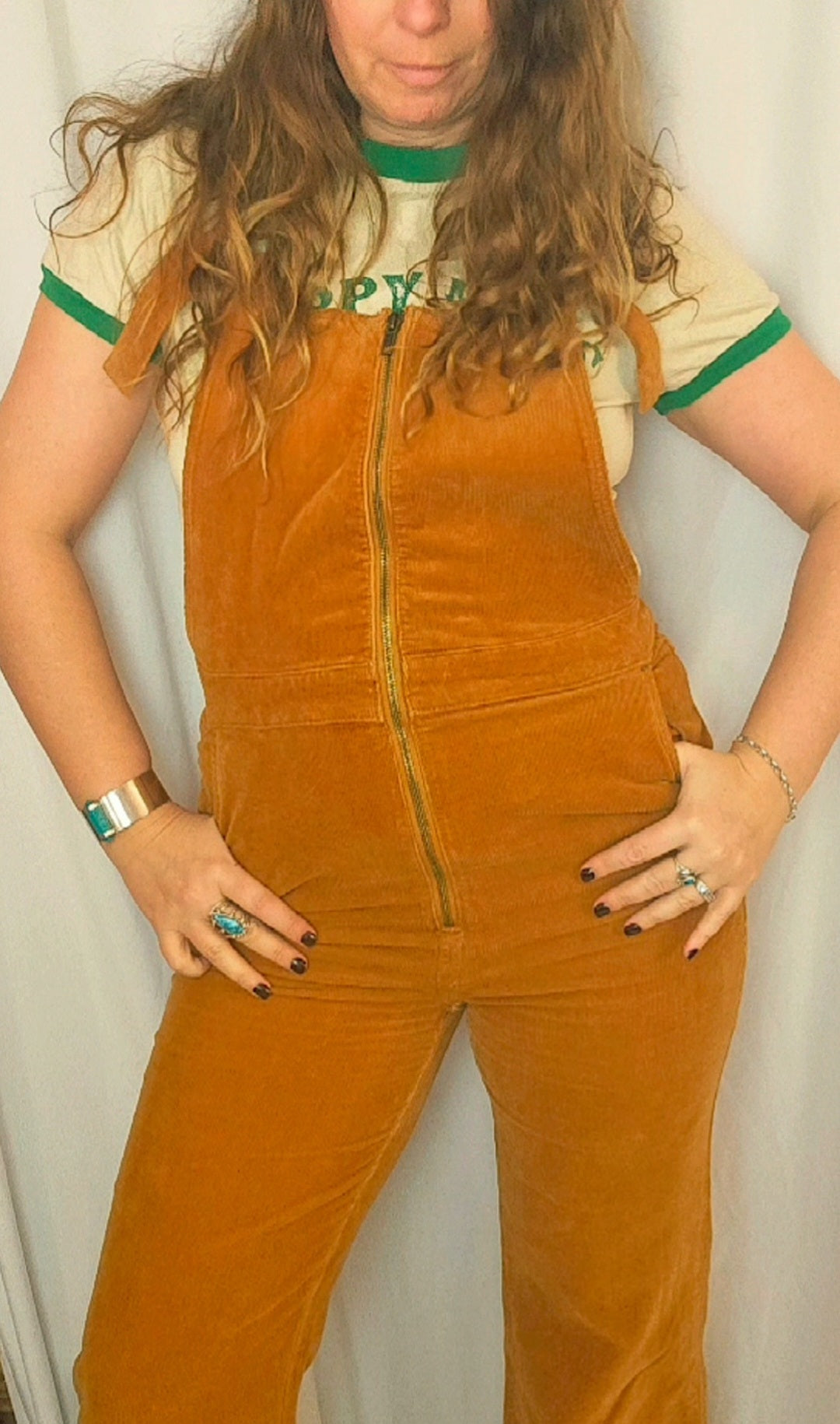 Person wearing a mustard yellow corduroy jumpsuit with a plain background