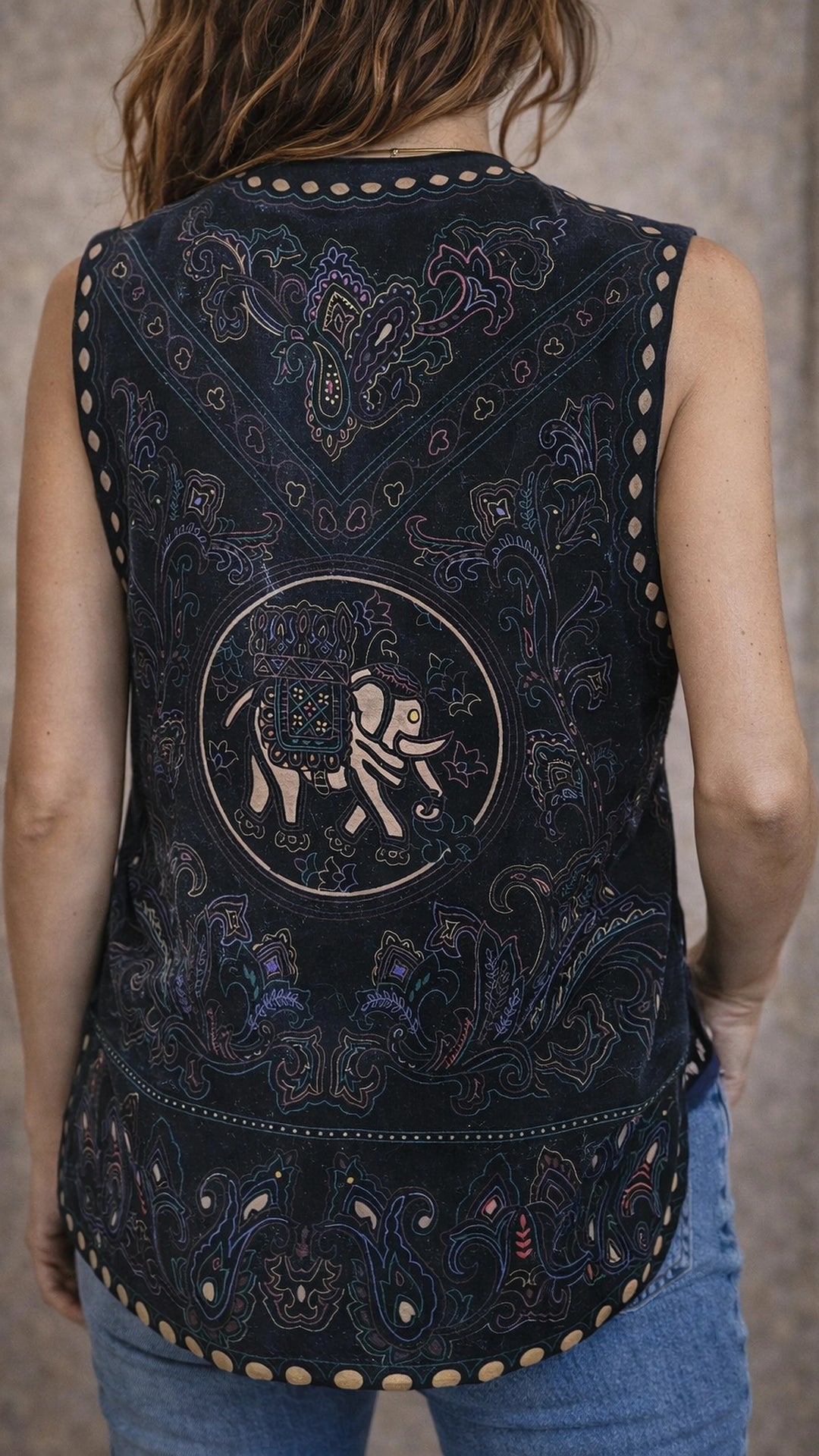 Black embroidered vest with intricate designs and a logo on the back, worn by a person.