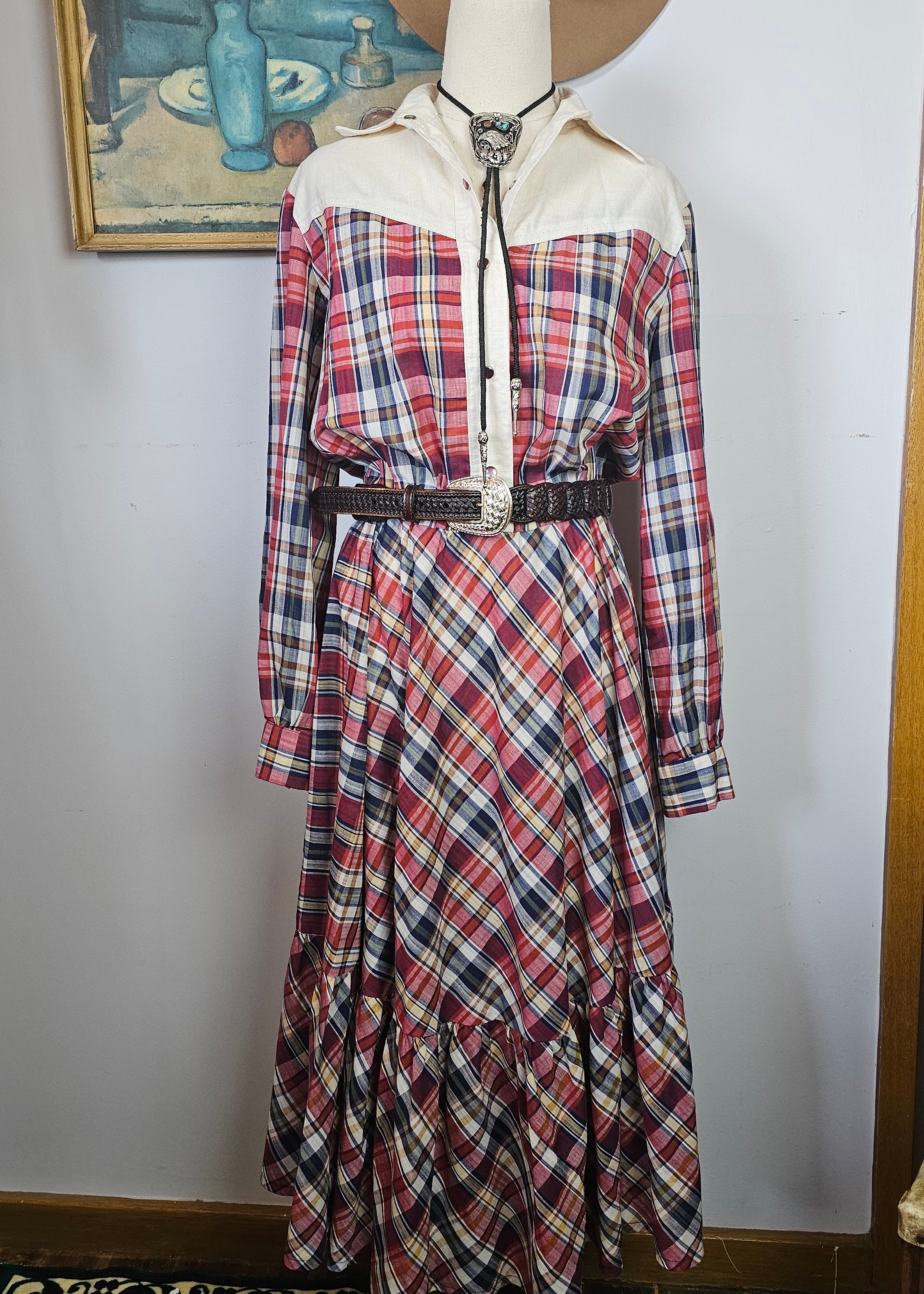 Plaid dress on a mannequin with a hat, against a white wall.
