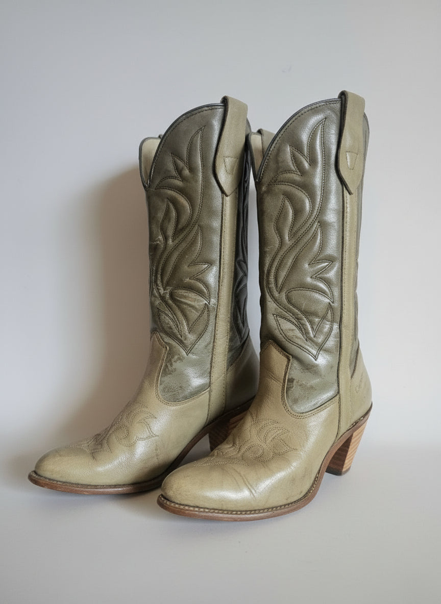 Pair of beige cowboy boots with intricate patterns on a textured white background