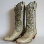 Pair of beige cowboy boots with intricate patterns on a textured white background