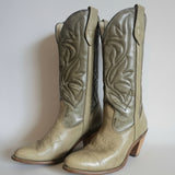 Pair of beige cowboy boots with intricate patterns on a textured white background