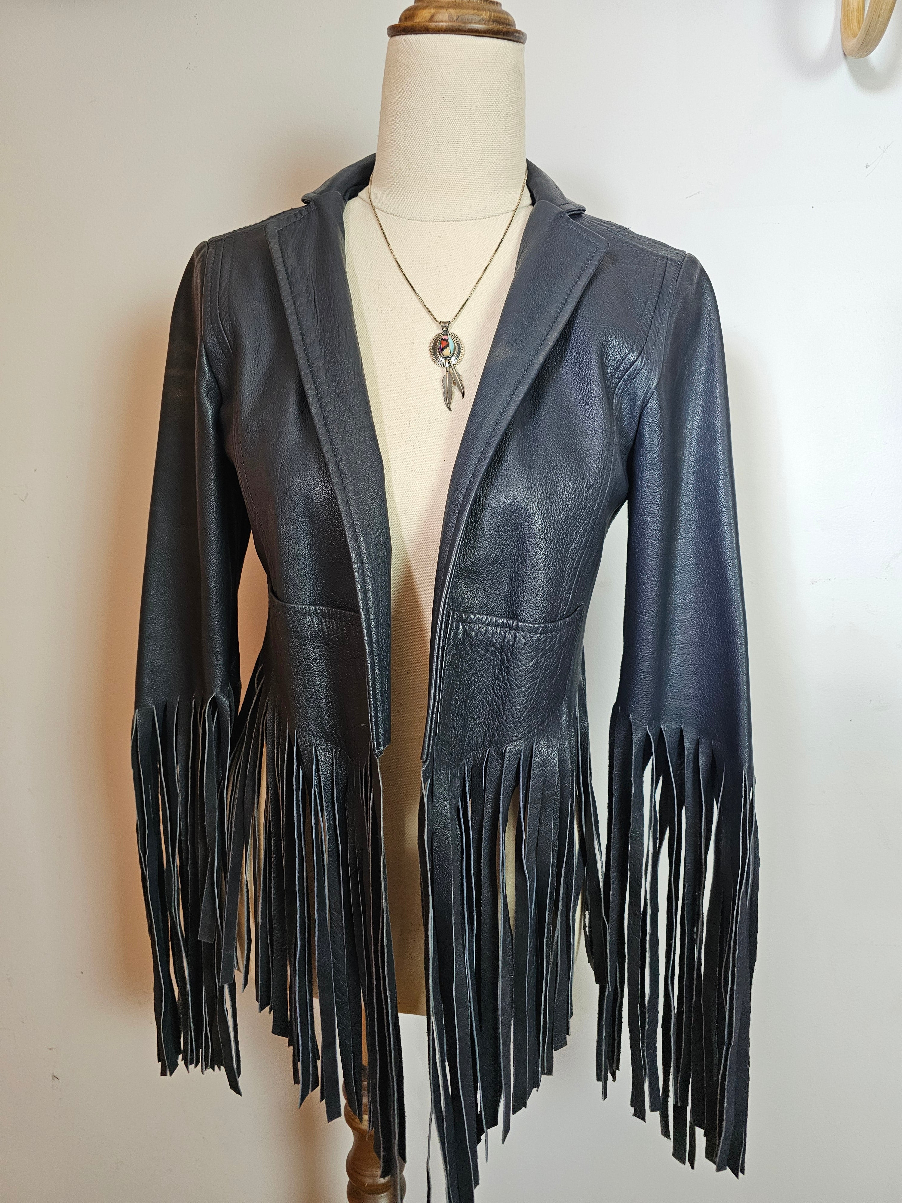 Black leather jacket with fringe on a mannequin against a white background