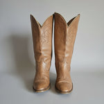 Pair of brown cowboy boots with intricate designs on a textured surface.
