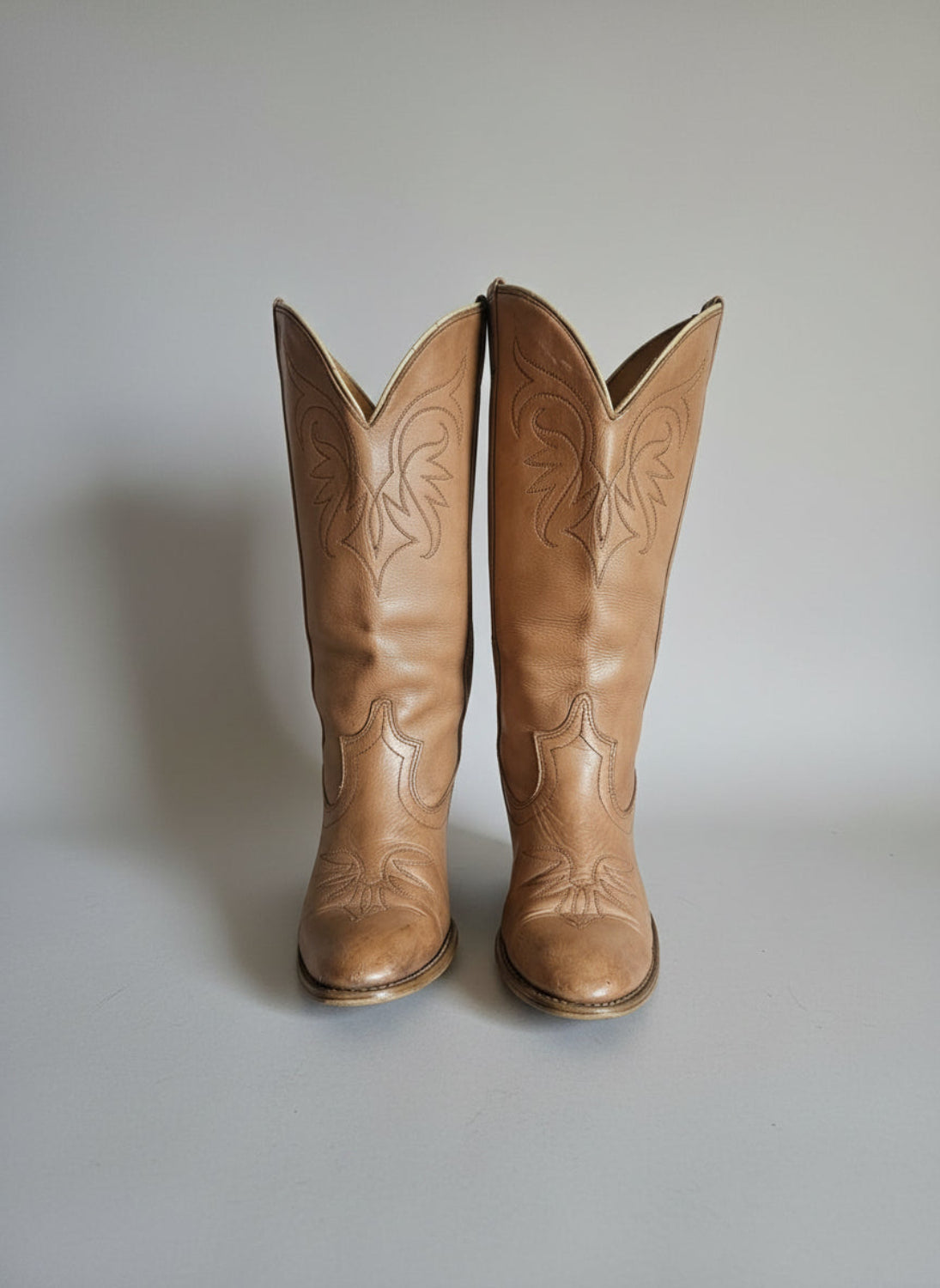Pair of brown cowboy boots with intricate designs on a textured surface.