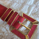 Red leather strap with gold buckle on a textured beige background