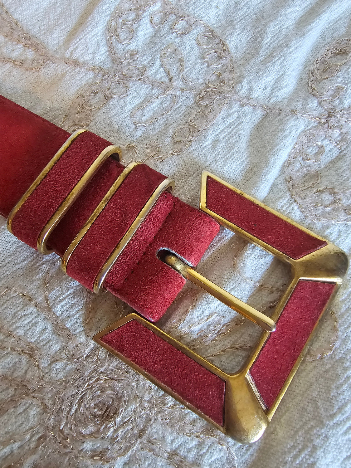 Red leather strap with gold buckle on a textured beige background
