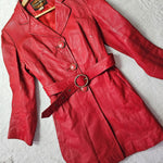 Flat lay of 1970s Stewart Hunt red leather trench coat with wide lapels, ring belt, and original buttons on white textured background.