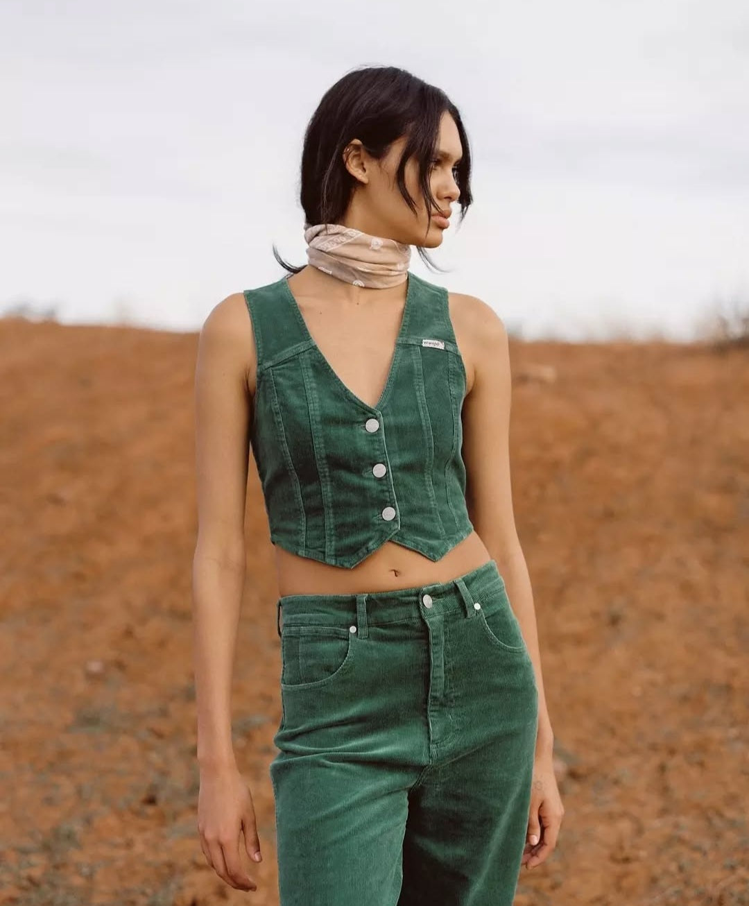 Woman wearing a green sleeveless top and pants in a desert-like setting