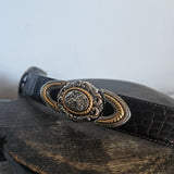 Close-up of a black leather bag with an ornate gold buckle on a light gray background