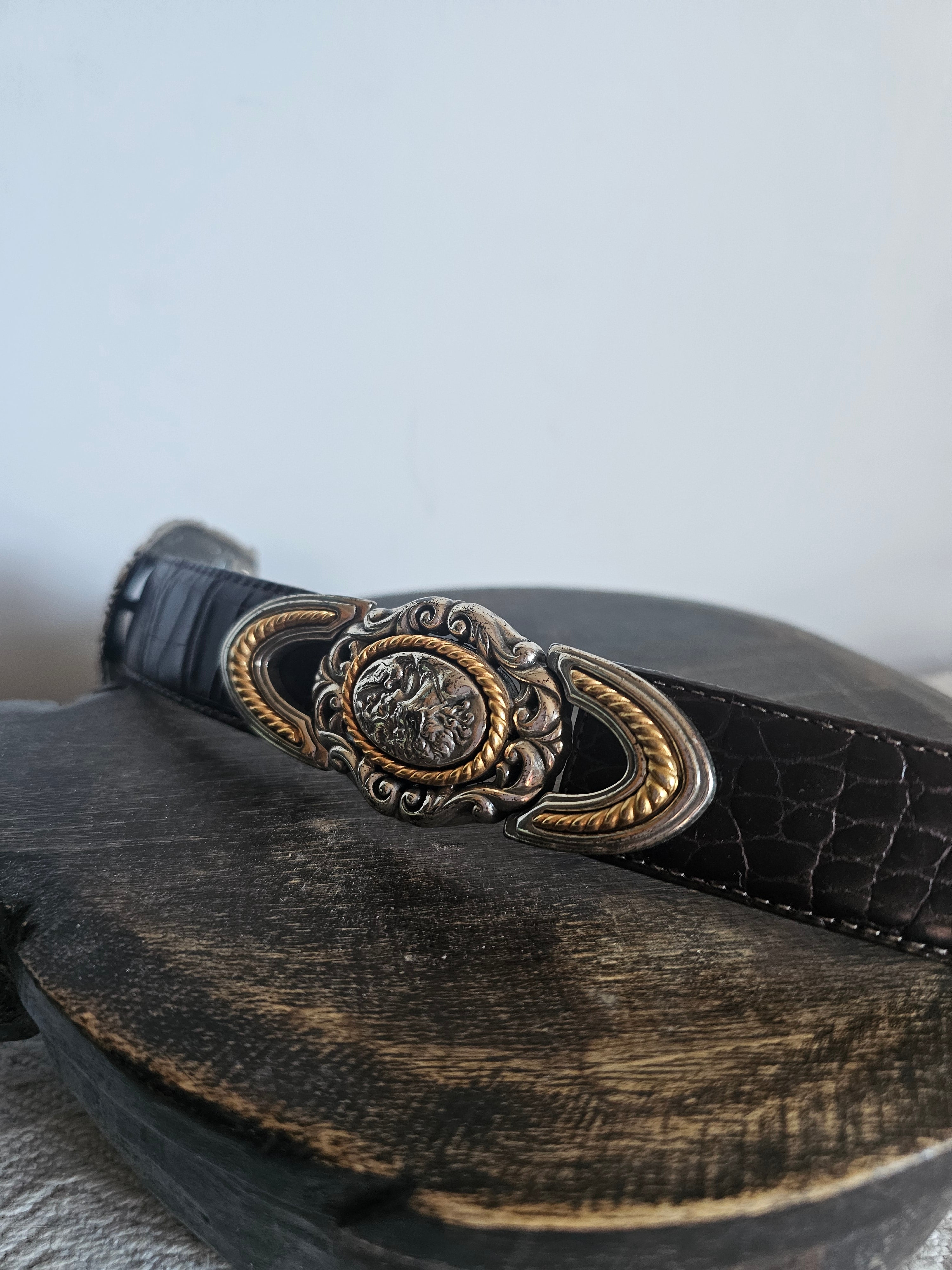 Close-up of a black leather bag with an ornate gold buckle on a light gray background