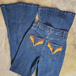 Folded blue jeans with rainbow designs on a textured beige surface