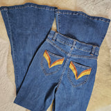 Folded blue jeans with rainbow designs on a textured beige surface