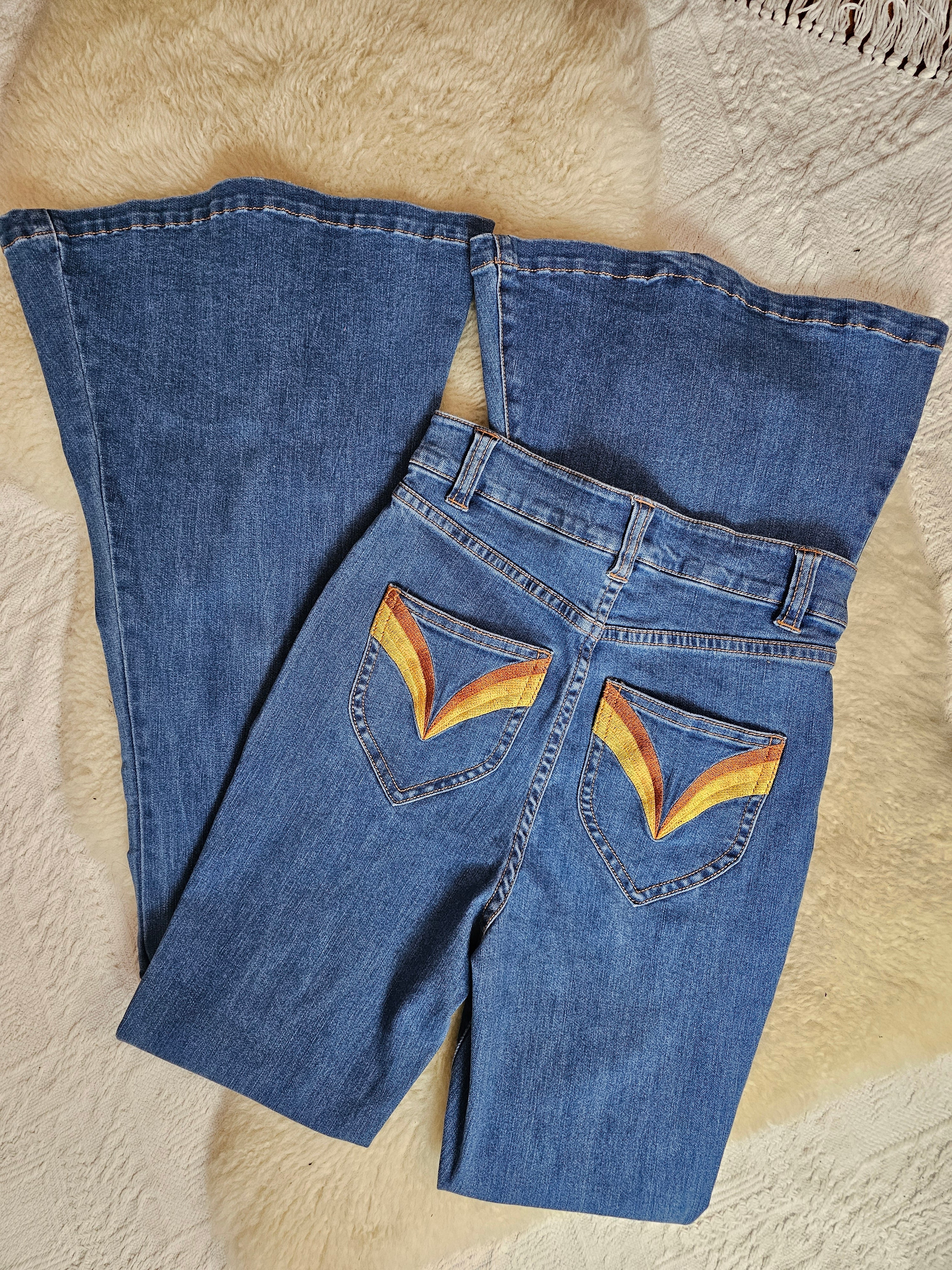 Folded blue jeans with rainbow designs on a textured beige surface
