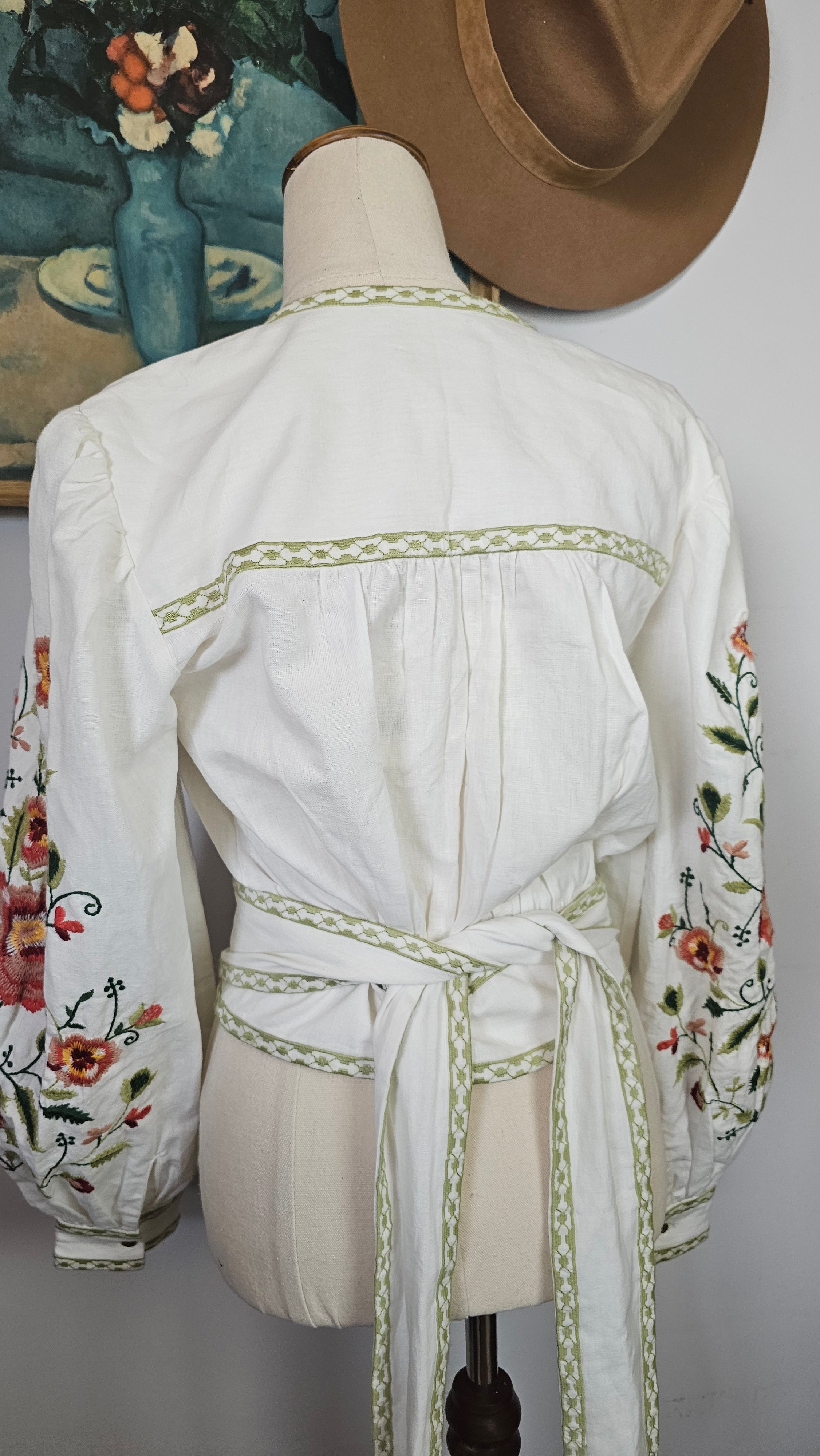 White embroidered dress on a mannequin with a brown hat and floral fabric in the background