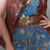 Person wearing a brown leather vest over a blue patterned dress with a gold belt.