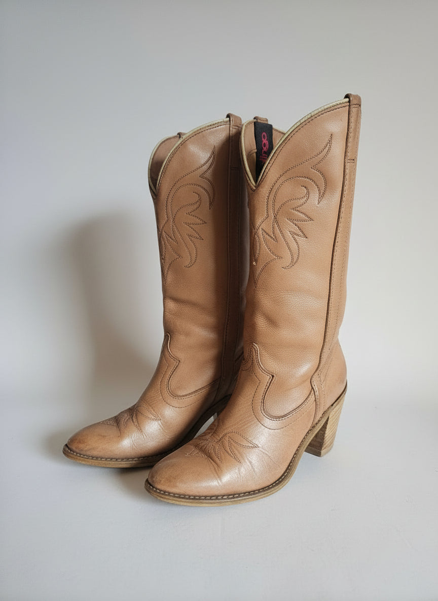 Pair of brown leather cowboy boots with intricate designs on a light background.