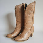 Pair of brown leather cowboy boots with intricate designs on a light background.