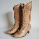 Pair of brown leather cowboy boots with intricate designs on a light background.