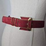 Close-up of a red leather belt with gold buckle on a beige background