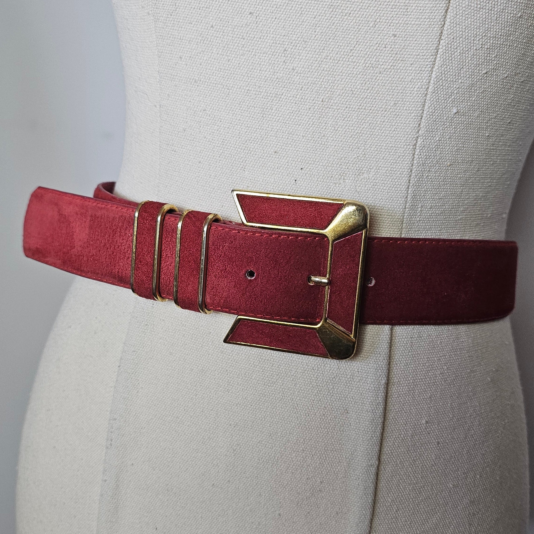 Close-up of a red leather belt with gold buckle on a beige background