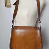 Brown leather handbag on a mannequin against a plain background