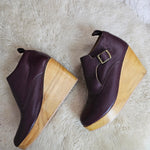 Pair of maroon shoes with wooden soles on a white fur surface
