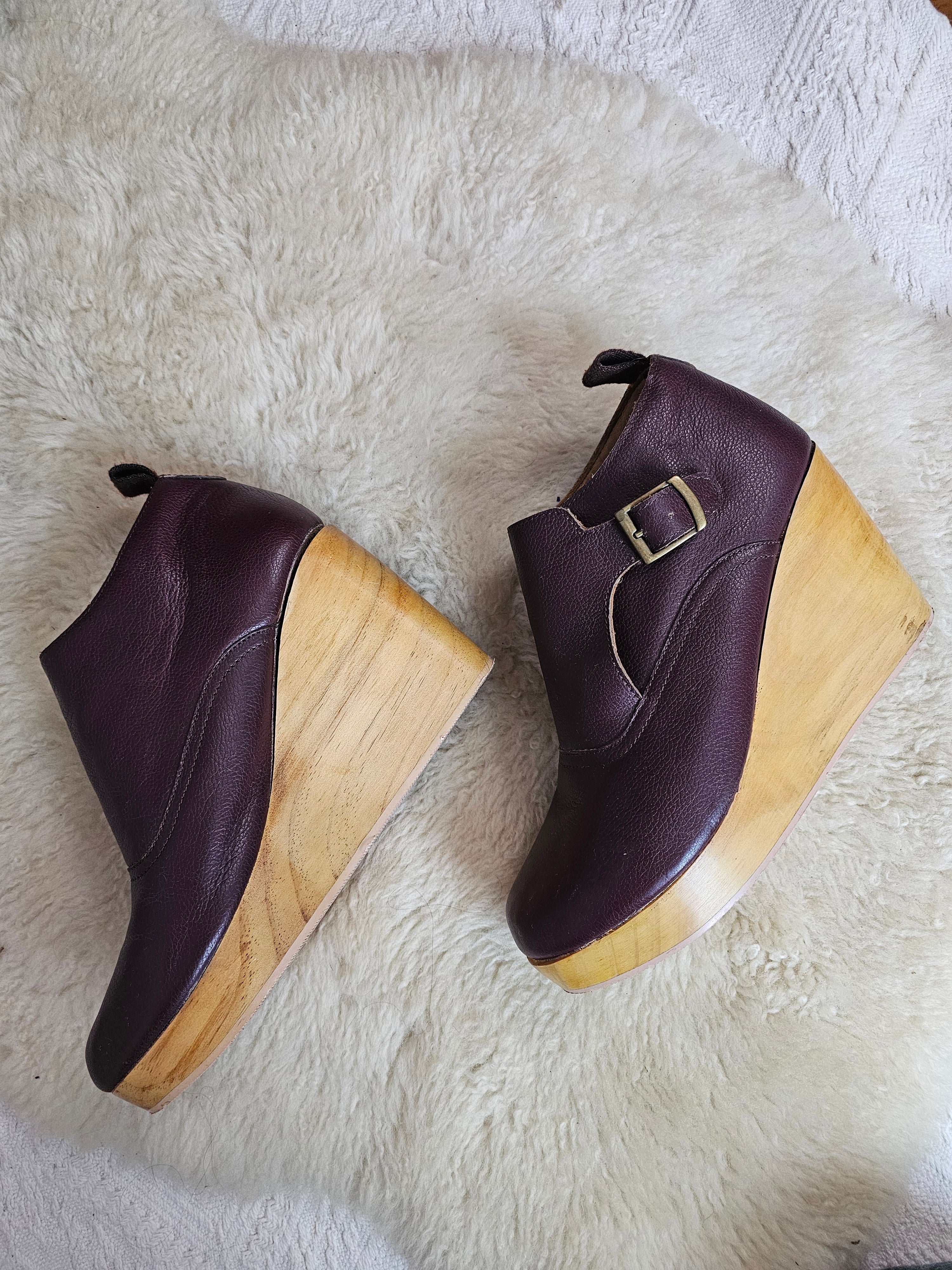 Pair of maroon shoes with wooden soles on a white fur surface