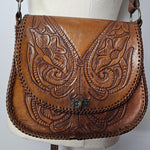 Brown leather handbag with intricate embossing on a white cushion