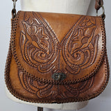 Brown leather handbag with intricate embossing on a white cushion