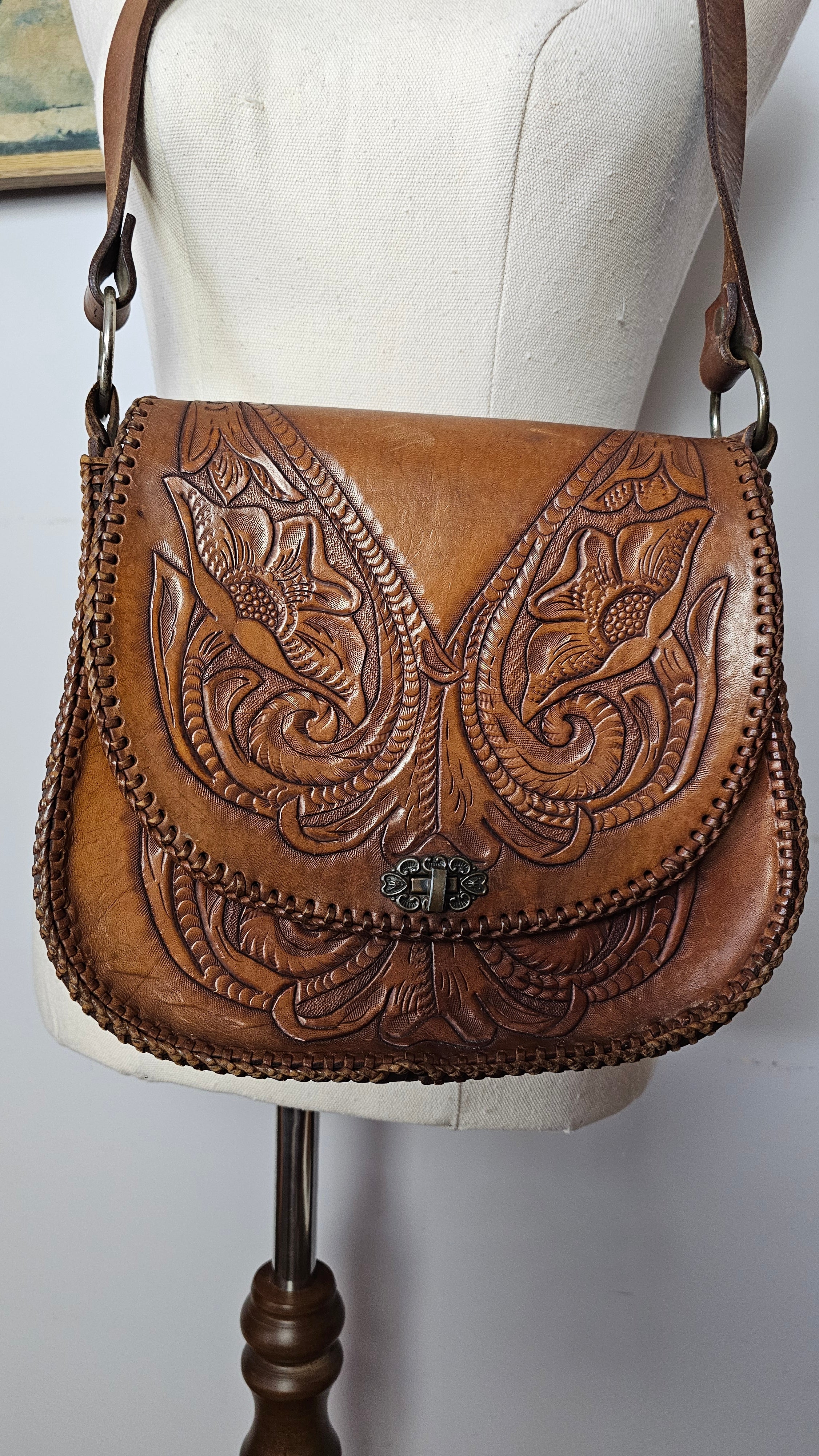 Brown leather handbag with intricate embossing on a white cushion
