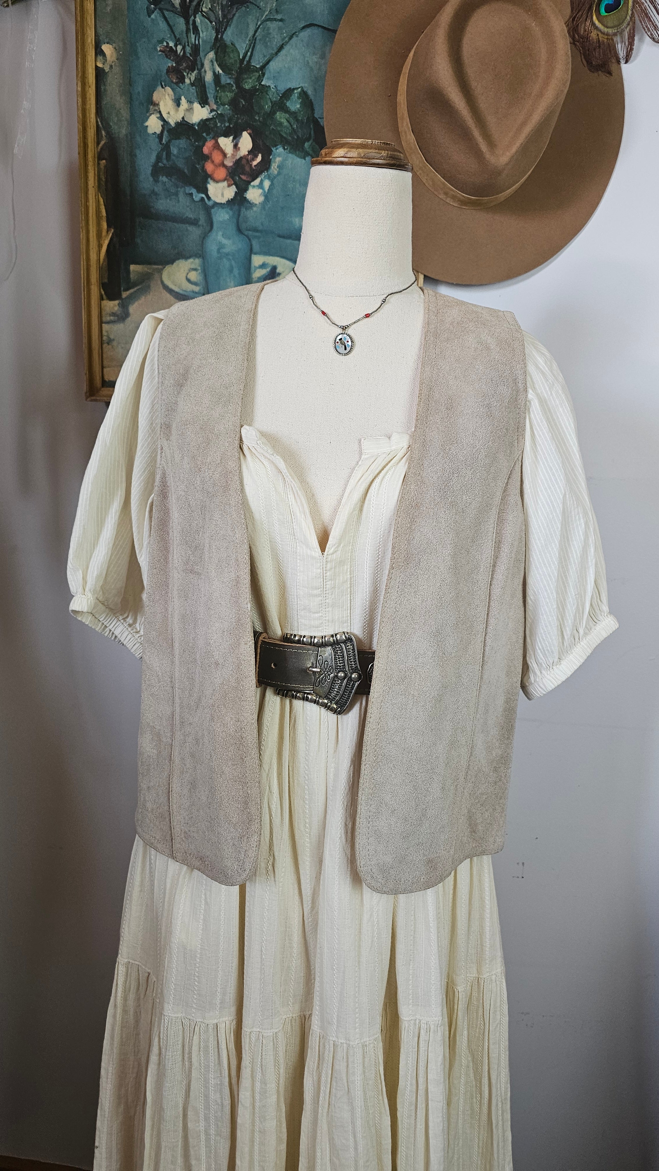 Mannequin wearing a beige trench coat with a hat and floral patterned fabric in the background