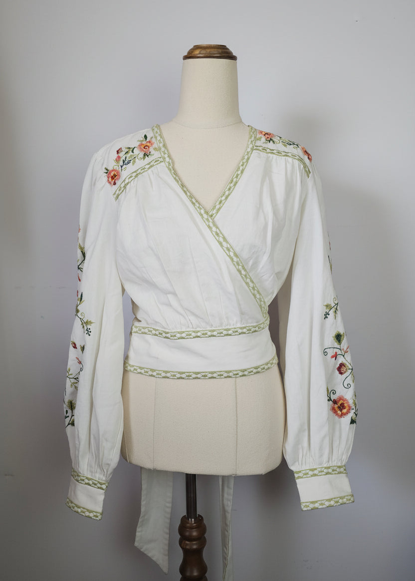 Traditional embroidered garment on a mannequin with a hat and fabric in the background