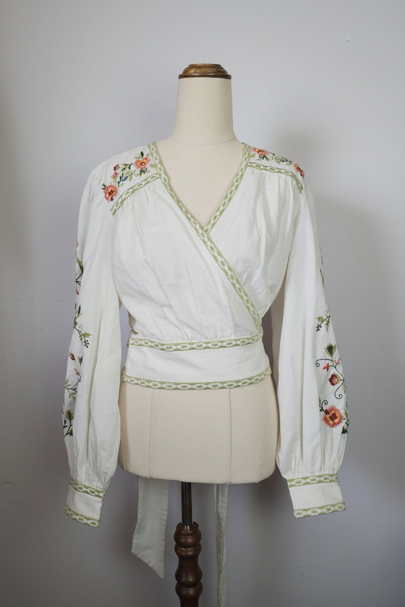 Traditional embroidered garment on a mannequin with a hat and fabric in the background