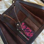 Brown leather bag with pink embroidery on a textured beige surface