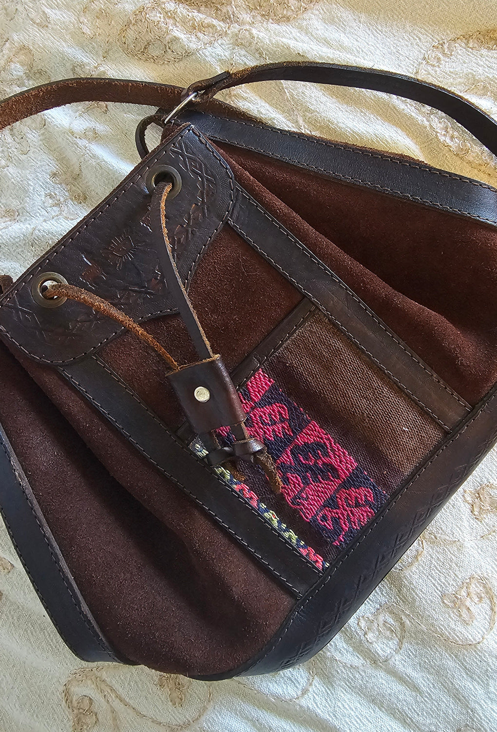 Brown leather bag with pink embroidery on a textured beige surface