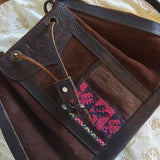 Brown leather bag with pink embroidery on a textured beige surface