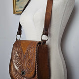 Close-up of a white saddle with brown leather girth and decorative pattern on a white background