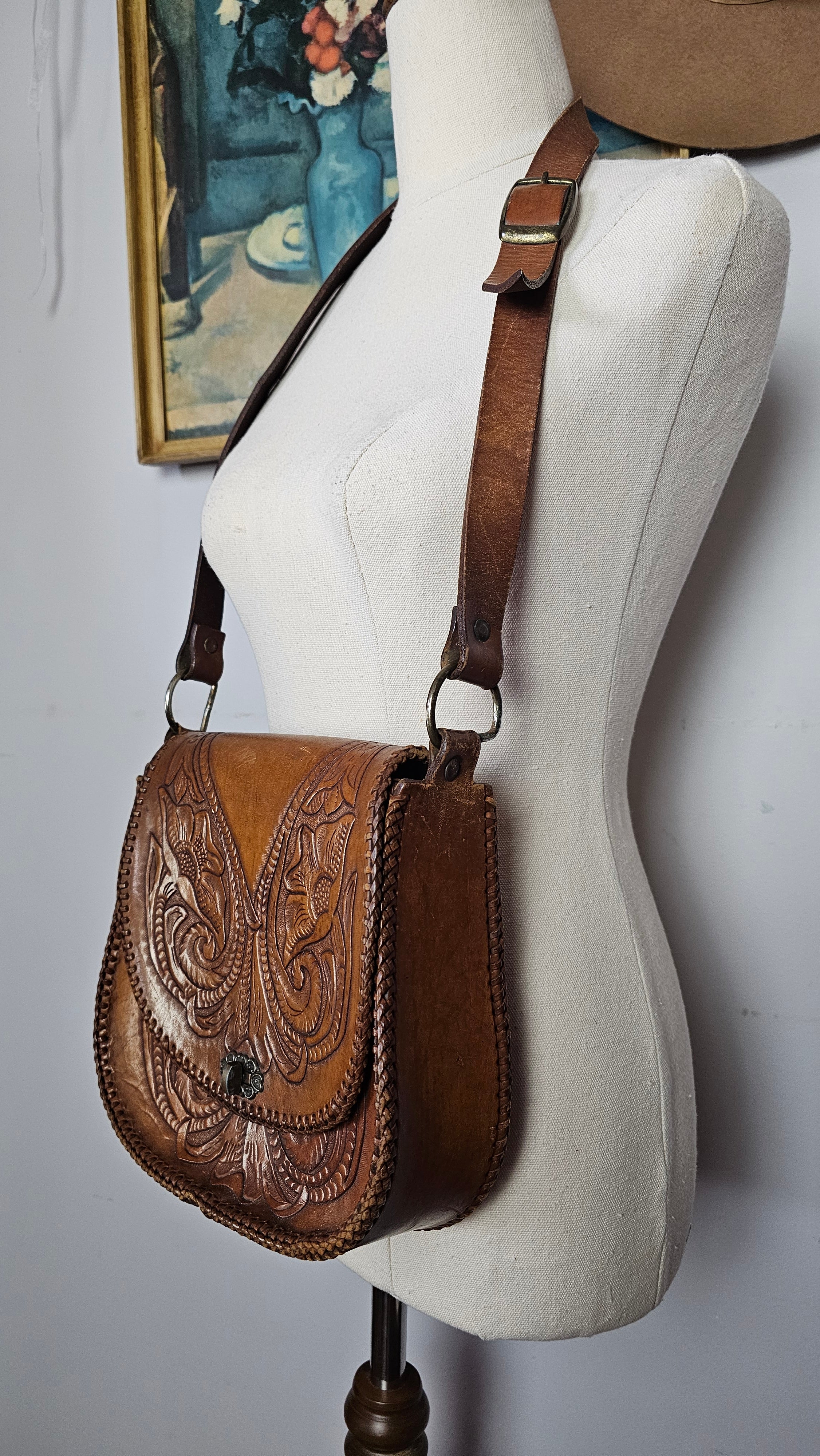 Close-up of a white saddle with brown leather girth and decorative pattern on a white background